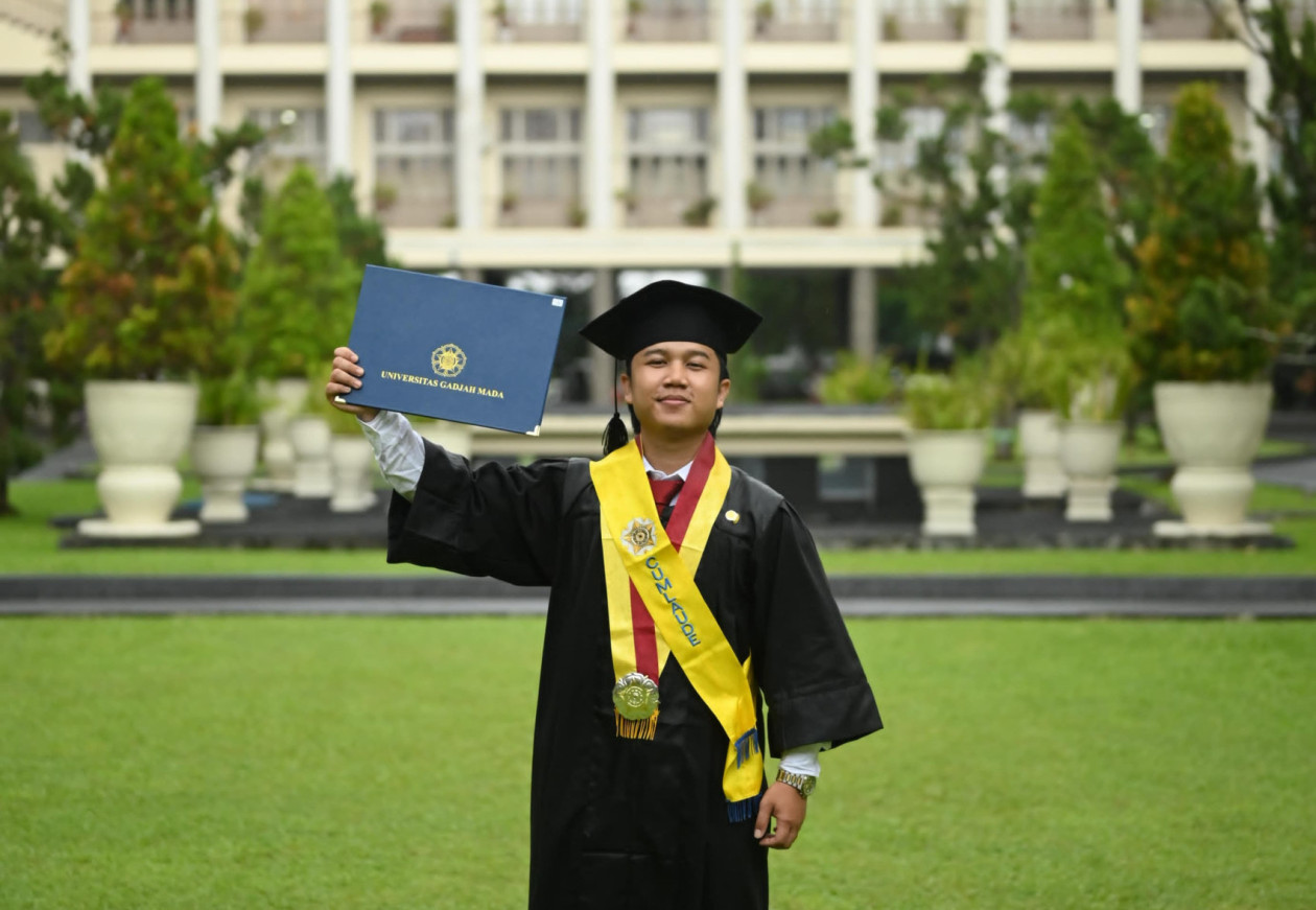 UGM law graduate Wahyu Aji Ramadan posing in his graduation gown after completing his degree with cum laude honors.